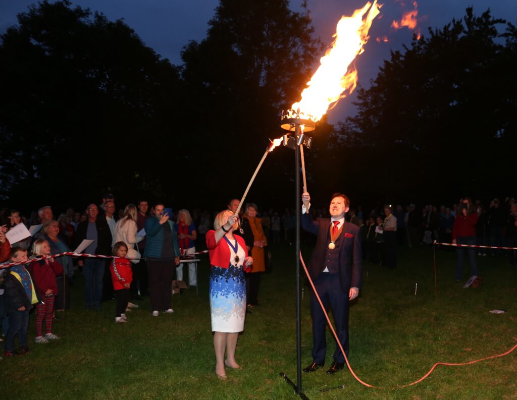 Photo of chairman of shavington cum gresty parish council and chair of shavington village festival committee lighting the beacon in the dark.